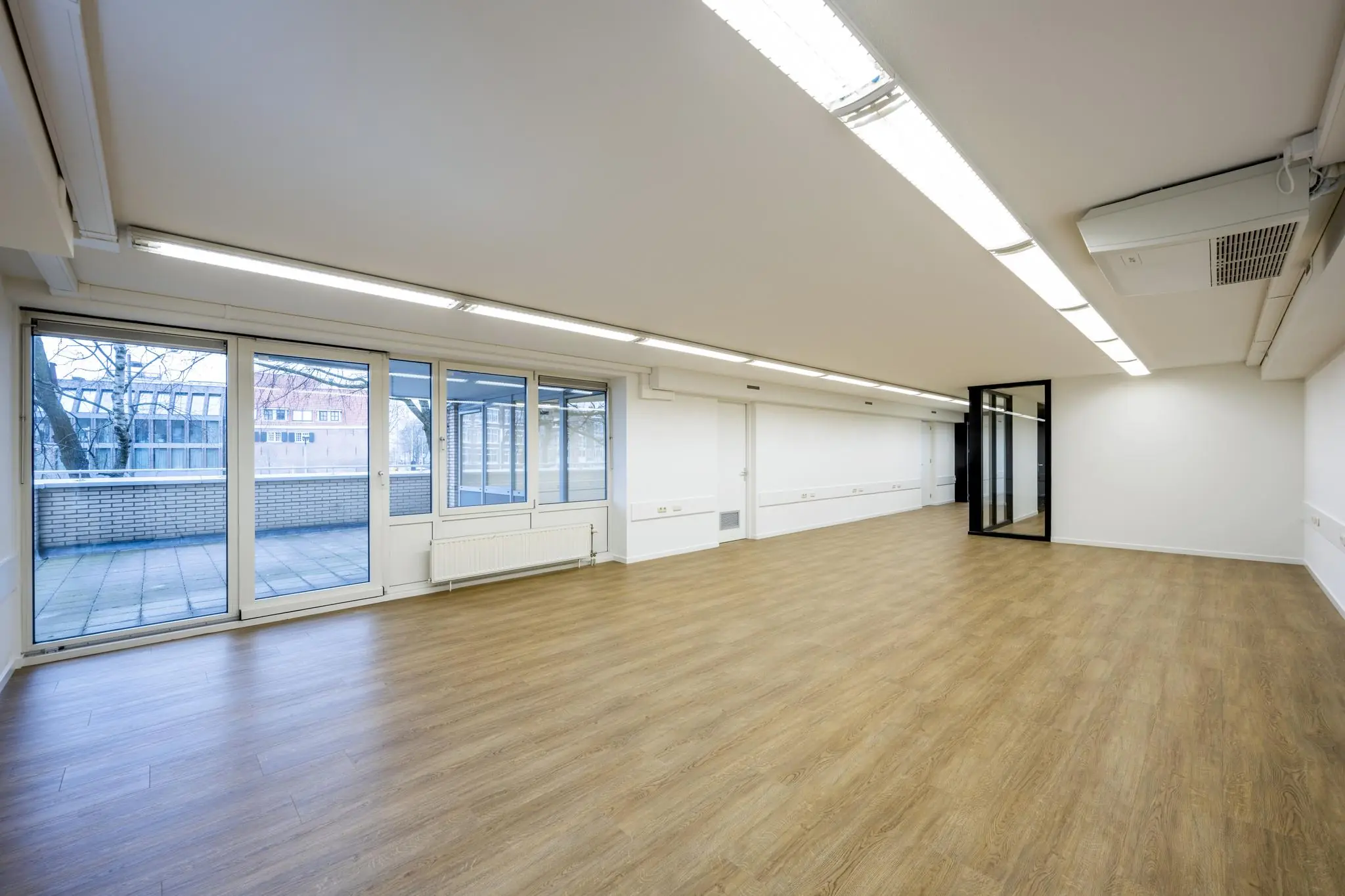 Lichte, lege kantoorruimte aan de Prins Hendrikkade met grote ramen, houten vloer en uitzicht op een ruim terras.